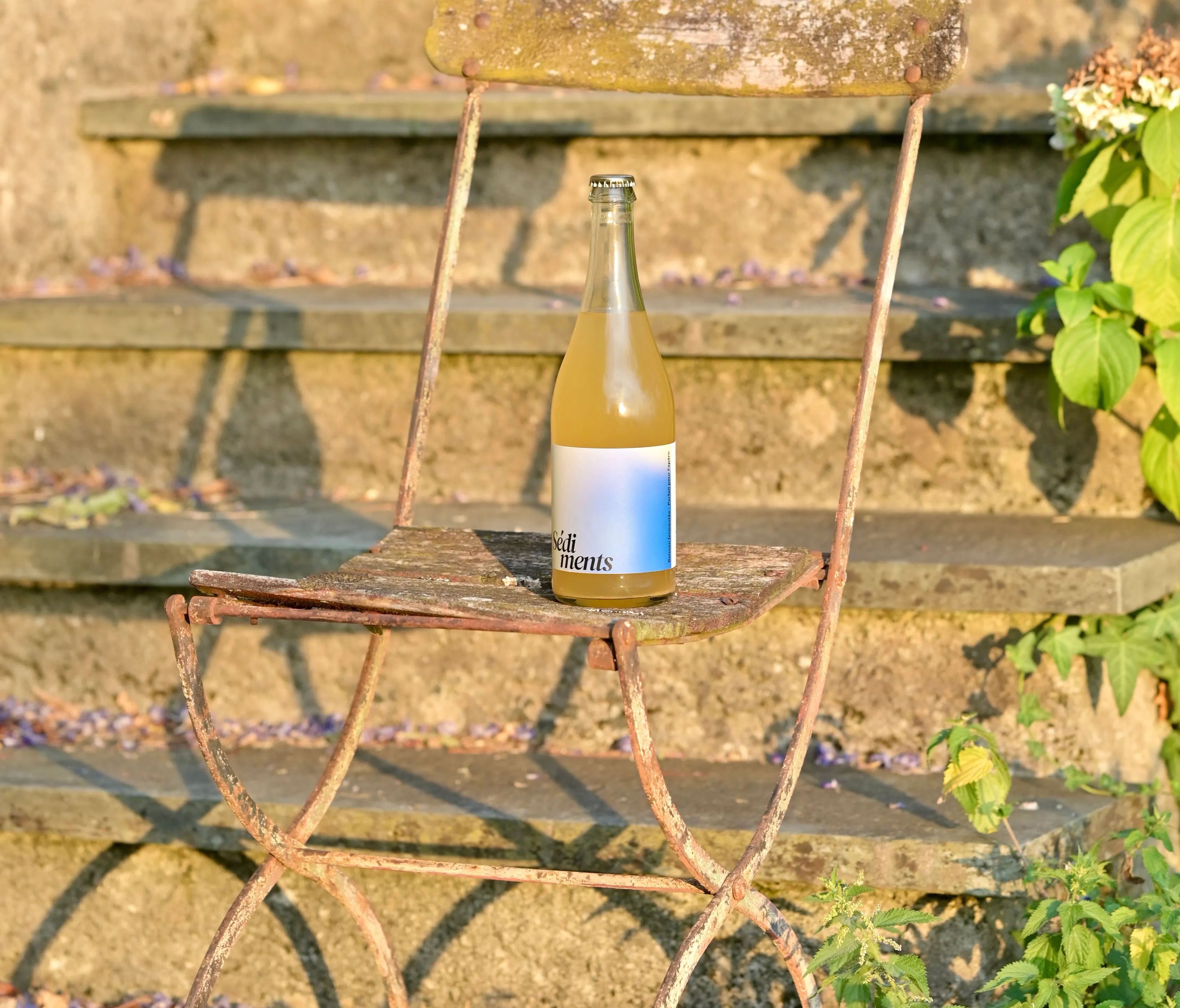 Bouteille Les prémices posée sur une chaise de jardin, en plein soleil